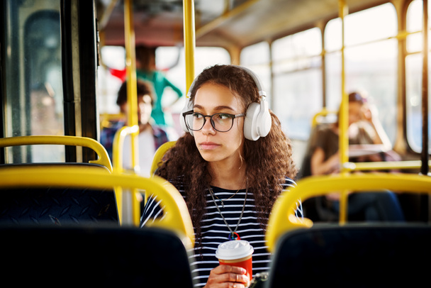 αξιολάτρευτο γυναίκα που κάθεται στο κάθισμα λεωφορείου ακούγοντας μουσική, και πίνεις καφέ  - Φωτογραφία, εικόνα
