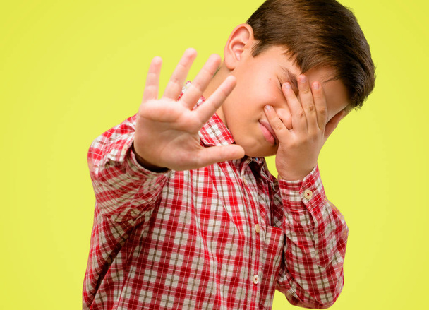 Beau tout-petit enfant aux yeux verts stressant et timide gardant la main sur la tête, fatigué et frustré sur fond jaune
 - Photo, image