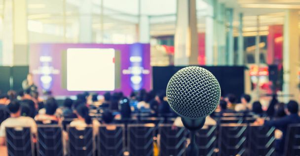 Микрофон над абстрактным размытым фото конференц-зала или зала семинара со спикерами на сцене и на фоне участников, Концепция бизнес-встреч
 - Фото, изображение