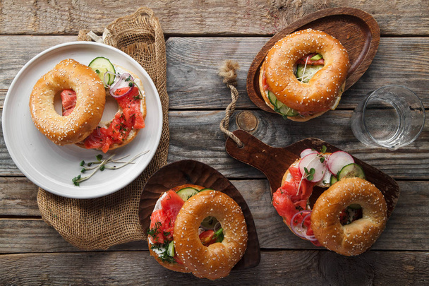 bagels with salmon fish and cream cheese with cucumber and fresh radish slices on plate and wooden cutting boards, close-up  - Φωτογραφία, εικόνα