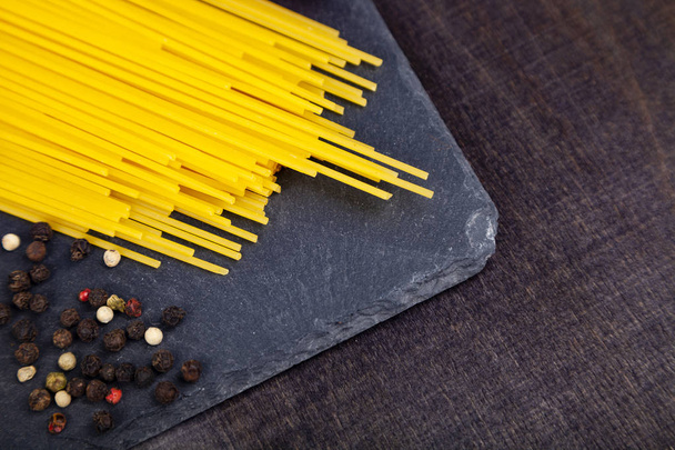Spaghetti and peppercorns on a dark wooden background - Photo, image