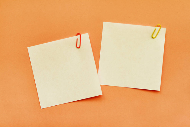 Two white adhesive note papers with clips on orange background - Fotografie, Obrázek