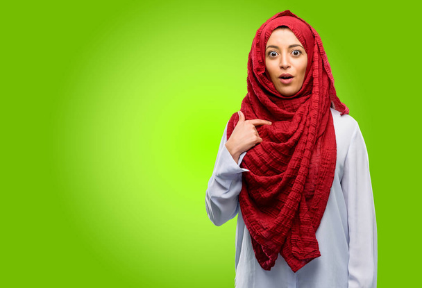 junge arabische Frau trägt Hijab glücklich und überrascht jubelnd ausdrückende Wow-Geste, zeigt mit dem Finger - Foto, Bild