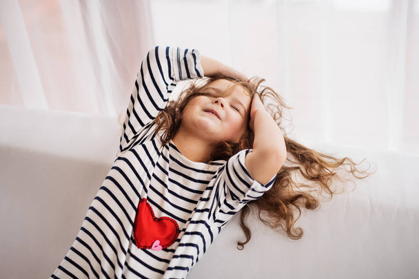 A small happy girl in striped T-shirt at home having fun. - Fotó, kép