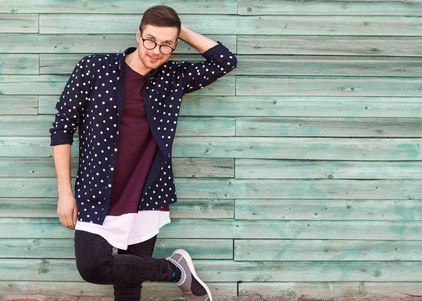 fashion guy hipster in fashion glasses posing on a wooden blue backgroun - Foto, Imagen