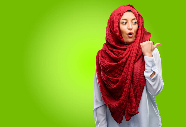 Fiatal arab nő visel a hidzsáb, boldog és meglepett ujjongott kifejező wow gesztus felfelé mutató - Fotó, kép