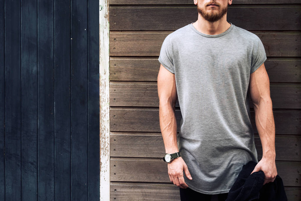 A cropped photo of a muscular male model wearing blank gray t-shirt while standing on a wooden background - Φωτογραφία, εικόνα