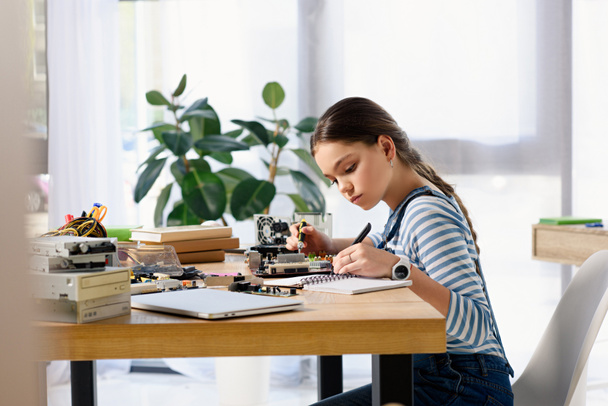 side view of adorable preteen child fixing computer motherboard and making notes at home - Photo, Image