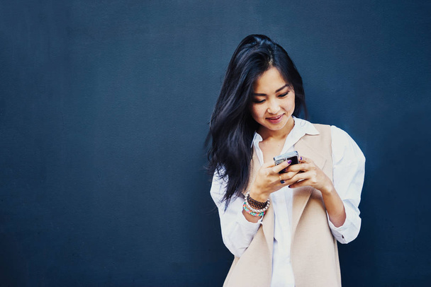 Portret of young Asian woman using smartphone on a black wall background  - Φωτογραφία, εικόνα