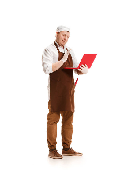Serious butcher posing with a laptop isolated on white background - Foto, immagini