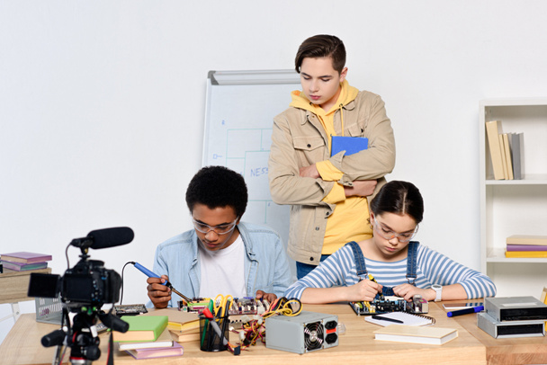 menino adolescente assistindo como amigos multiculturais soldando circuito de computador com ferro de solda em casa
 - Foto, Imagem