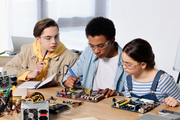 πολυπολιτισμική έφηβοι συγκόλληση υπολογιστή κυκλώματος με κολλητήρι στο σπίτι - Φωτογραφία, εικόνα