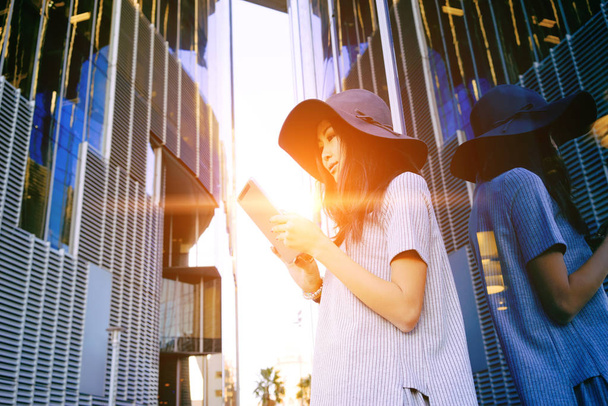 Young stylish Asian businesswoman using digital tablet near skyscrapers - Фото, изображение