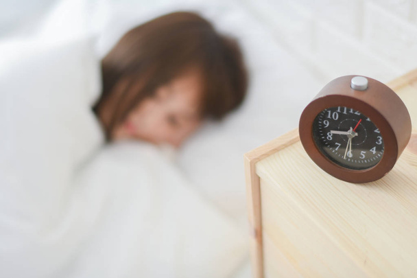 Mujer durmiendo en la cama tranquilamente en casa al lado del despertador
 - Foto, Imagen