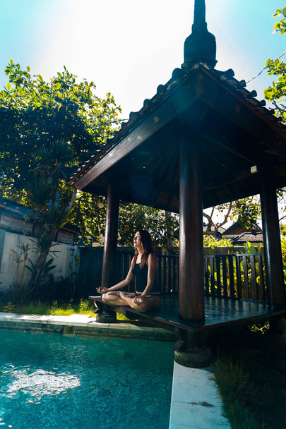 Vrouwelijke mediteren bij het zwembad, Bali, Indonesia.The meisje zit in een prieel op een bali in een lotus houding en mediteert met een uitzicht op het zwembad. - Foto, afbeelding