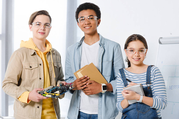 adolescentes multiculturais segurando placa-mãe de computador e livros em casa
 - Foto, Imagem