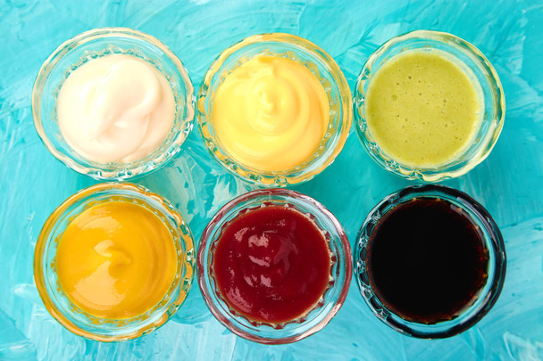 Conjunto de molhos diferentes. Molhos ketchup, mostarda, maionese, wasabi, molho de soja em pequenas tigelas em fundo azul
 - Foto, Imagem