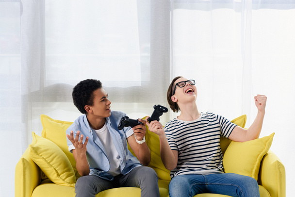 multicultural adolescente chicos mostrando sí gestos al ganar el videojuego en casa
 - Foto, Imagen