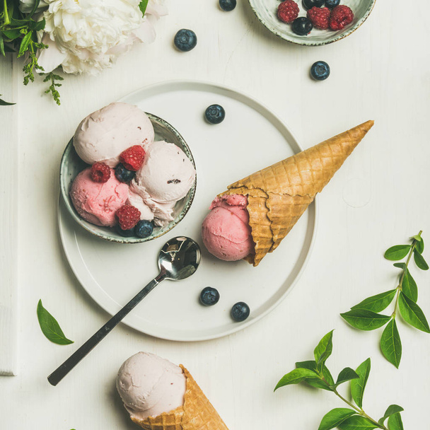 Pink strawberry and coconut ice cream scoops in bowl, sweet waffle cones, peony flowers bouquet and fresh berries over white background - Foto, Imagem