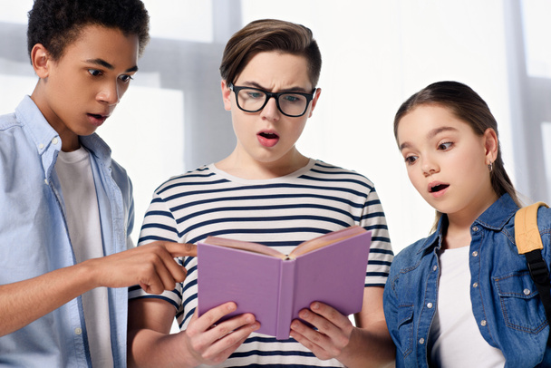 adolescentes multiculturales sorprendidos mirando el libro en casa
 - Foto, imagen