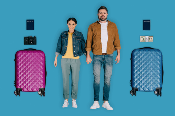 top view of young couple of stylish travelers with passports, money, photo camera and suitcases isolated on blue background - Zdjęcie, obraz