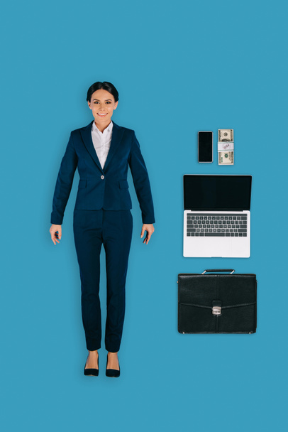 top view of businesswoman with laptop, briefcase, money and smartphone isolated on blue background - Fotó, kép