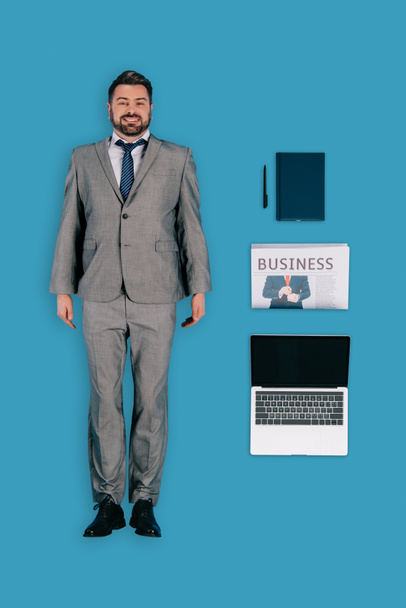 Widok z góry biznesmena z laptopa, gazety, Podręcznik i pióra na białym tle na niebieskim tle - Zdjęcie, obraz