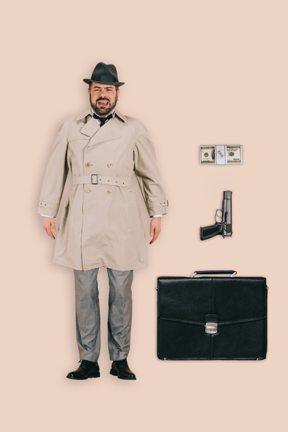 top view of male killer in hat with handgun, money and briefcase isolated on pink background - Photo, Image