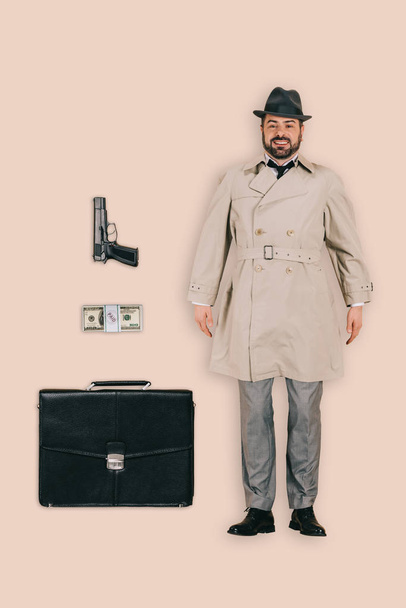 top view of male killer in hat with handgun, money and briefcase isolated on pink background - Φωτογραφία, εικόνα
