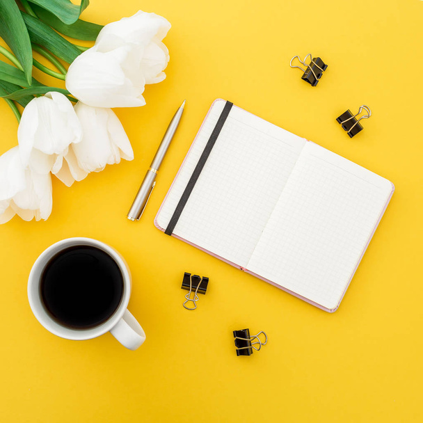 Вид сверху блокнота с чашкой кофе и белыми тюльпанами на желтом фоне
 - Фото, изображение