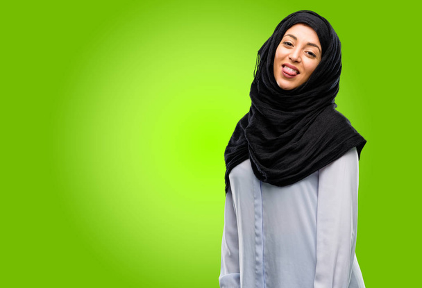 Jovem árabe mulher vestindo hijab salientando a língua na câmera em sinal de desobediência, protesto e desrespeito
 - Foto, Imagem