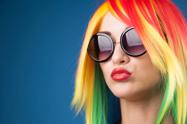 beautiful young woman wearing color wig and sunglasses against blue background - 写真・画像