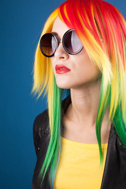 beautiful young woman wearing color wig and sunglasses against blue background - 写真・画像