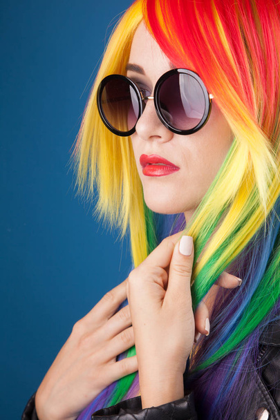 beautiful young woman wearing color wig and sunglasses against blue background - Foto, Imagem