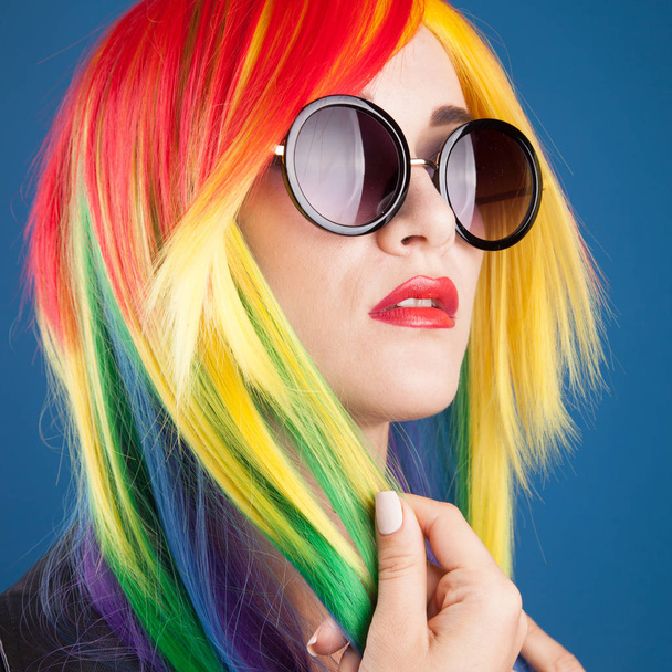 beautiful young woman wearing color wig and sunglasses against blue background - Фото, зображення
