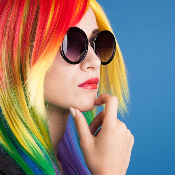 beautiful young woman wearing color wig and sunglasses against blue background - Foto, immagini