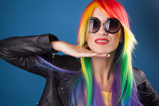 beautiful young woman wearing color wig and sunglasses against blue background - Foto, immagini