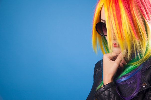 beautiful young woman wearing color wig and sunglasses against blue background - Fotografie, Obrázek