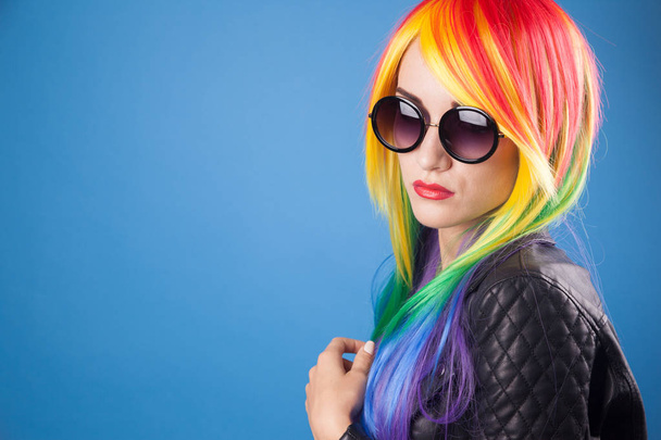 beautiful young woman wearing color wig and sunglasses against blue background - Foto, imagen