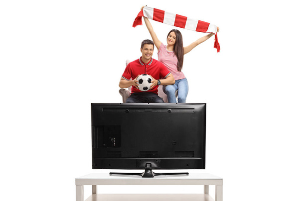 Cheerful soccer fans seated in an armchair watching a game of football on TV isolated on white background - Valokuva, kuva