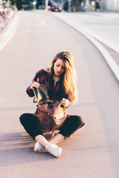 young woman sitting on skateboard searching in the bag - Foto, imagen