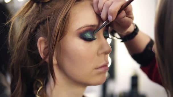 Make-up artist applies some colour shadows on models eyelids. Side view - Materiał filmowy, wideo