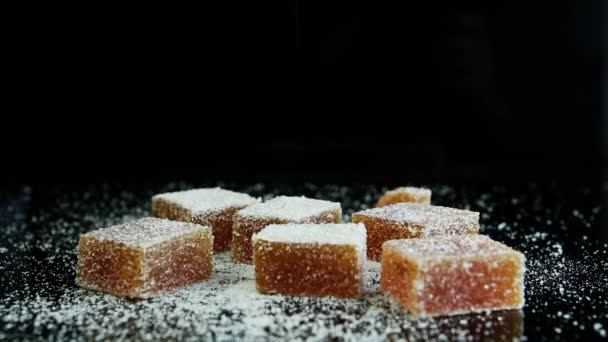 kleine Marmeladenteile fallen auf verstreute orangefarbene Marmeladengruppe mit Zucker auf schwarzem Spiegelhintergrund - Filmmaterial, Video