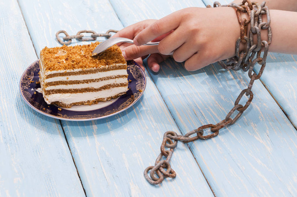 dziewczynka jedzenie pyszne ciasto na jasno niebieskim tle. Ręce związane z łańcuchami. - Zdjęcie, obraz