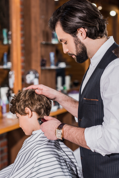 adorable rizado chico consiguiendo corte de pelo de peluquero con Hair Clipper
 - Foto, Imagen