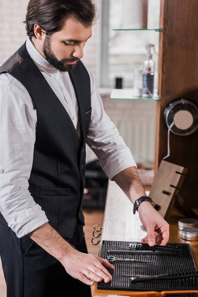 handsome young barber taking tools from rubber mat on workplace - Foto, Bild