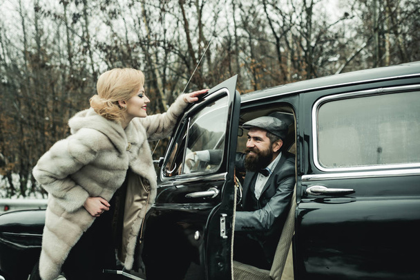 Bearded man and sexy woman in fur coat. Couple in love on romantic date. Travel and business trip or hitch hiking. Retro collection car and auto repair by mechanic driver. Escort of girl by security - Photo, image