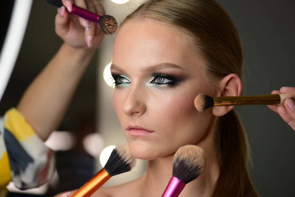 Closeup portrait young woman has around face brushes for different types of makeup - Foto, imagen