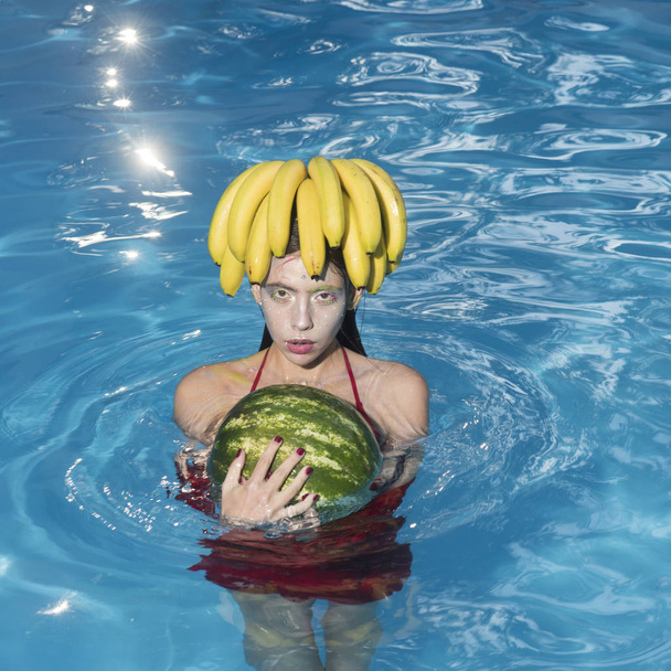 Girl on beach hold watermelon and banana in the blue pool. Tropical fruit diet. Summer holiday idyllic. - Foto, imagen