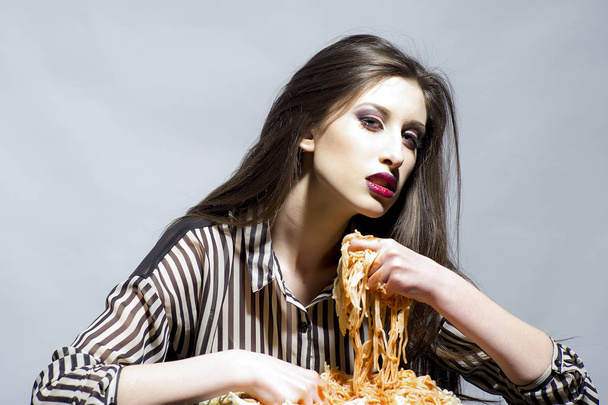 Schoonheid model met make-up en lang donkerbruine haren hebben diner. Sexy vrouw eten spaghetti met handen. Vrouw eet pasta schotel met tomatenketchup. Hongerig meisje hebben Italiaanse maaltijd. Voedsel, voeding en keuken. - Foto, afbeelding